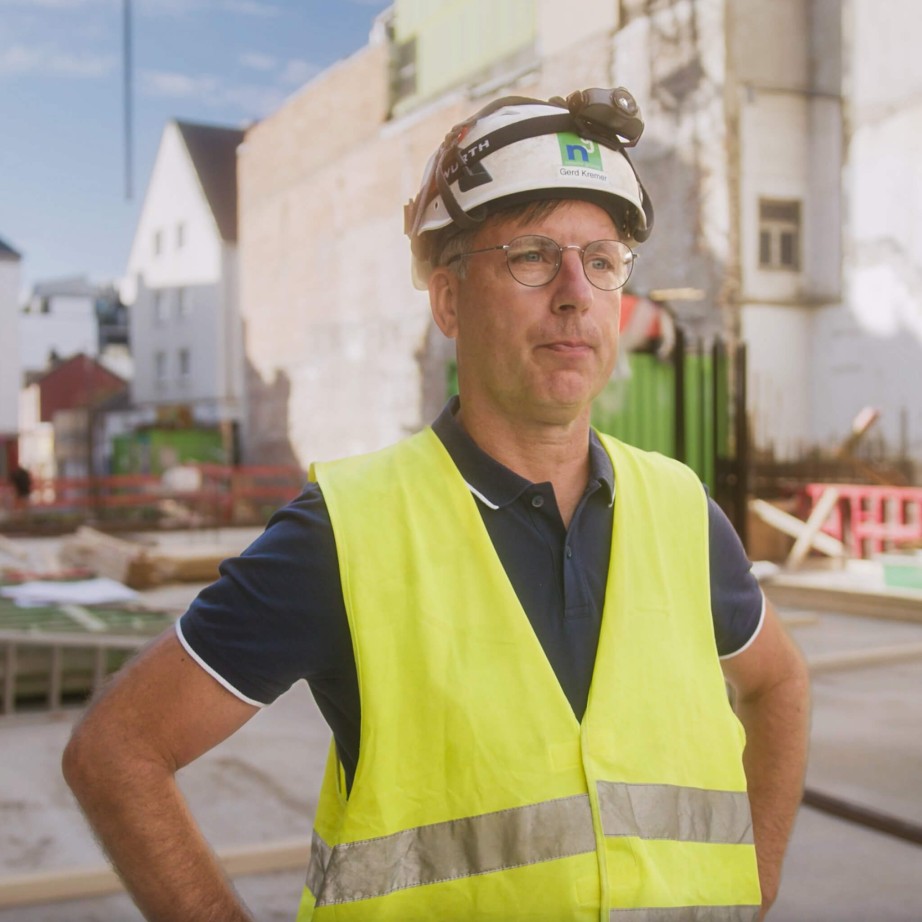 Bauleiter der Firma Nesseler auf der Baustelle und erklärt die Bausoftware Vorteile. Im Hintergrund ist seine Baustelle zu sehen.