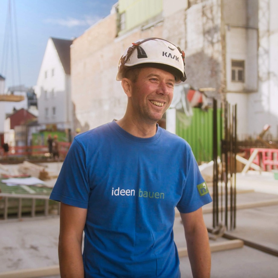 Polier der Firma Nesseler in Sicherheitsausrüstung auf der Baustelle mit der Bausoftware von specter automation. Im Hintergrund sind Baustelle und Häuser zu erkennen, die Sonne scheint.