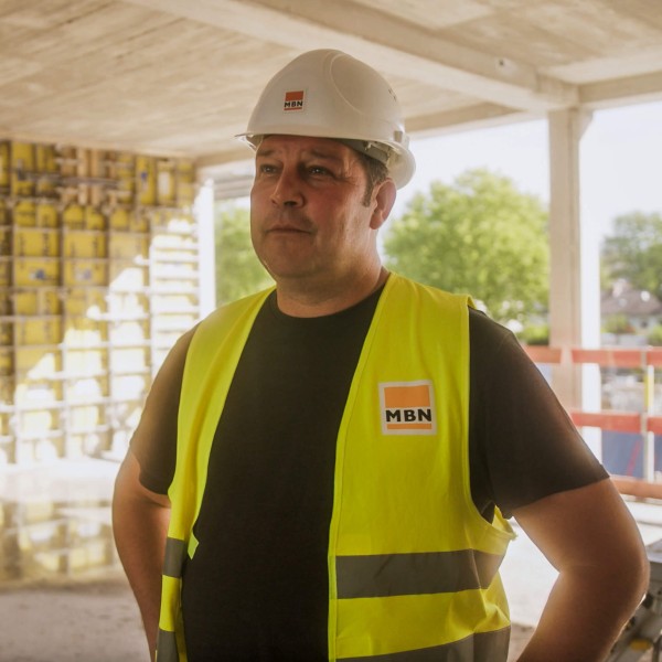 Ein Polier in Warnweste steht auf einer sonnigen Baustelle und nutzt specter automation, eine Baumanagement Software.