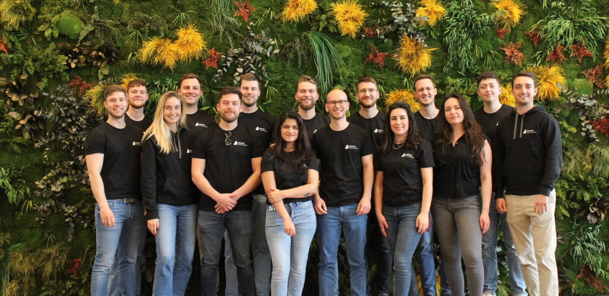 Das specter automation Team steht als Gruppe vor einer grünen Wand und macht auf den Startup Job aufmerksam.